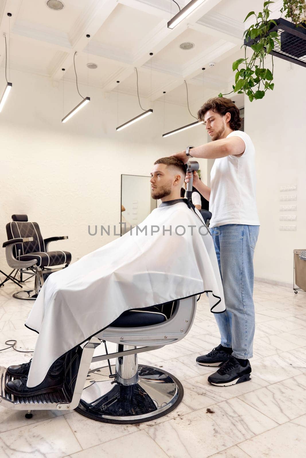 Professional hairdresser during work with man client with hair dryer in barber shop. Haircut in the barbershop.