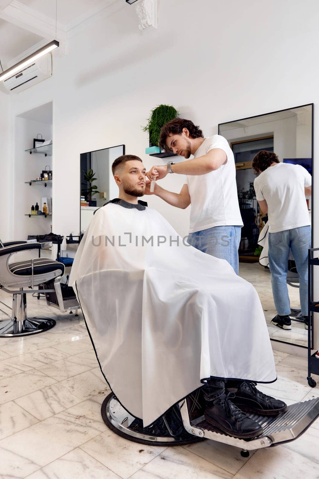 Hairstylist serving handsome man in barber shop. by erstudio