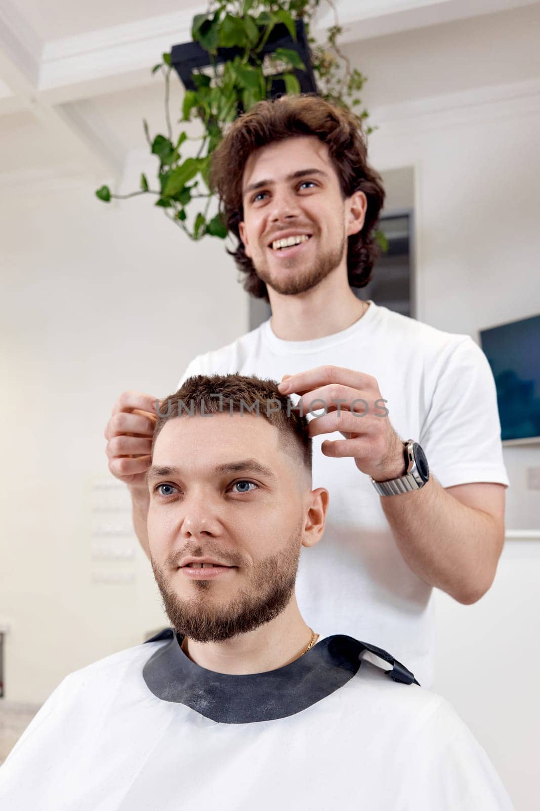 Barber and satisfied bearded man in front of the mirror in barber shop