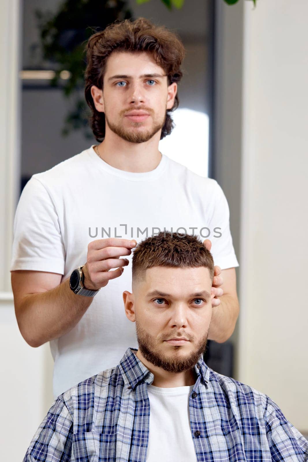 Barber and satisfied bearded man in front of the mirror in barber shop