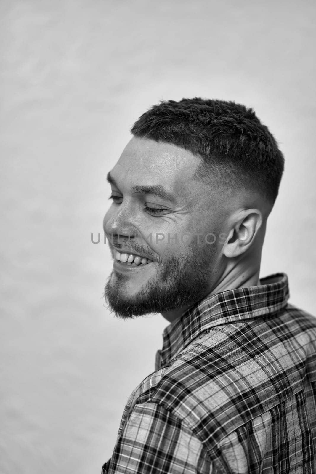 happy young man with stylish hair and beard in a plaid shirt on gray background. black and white