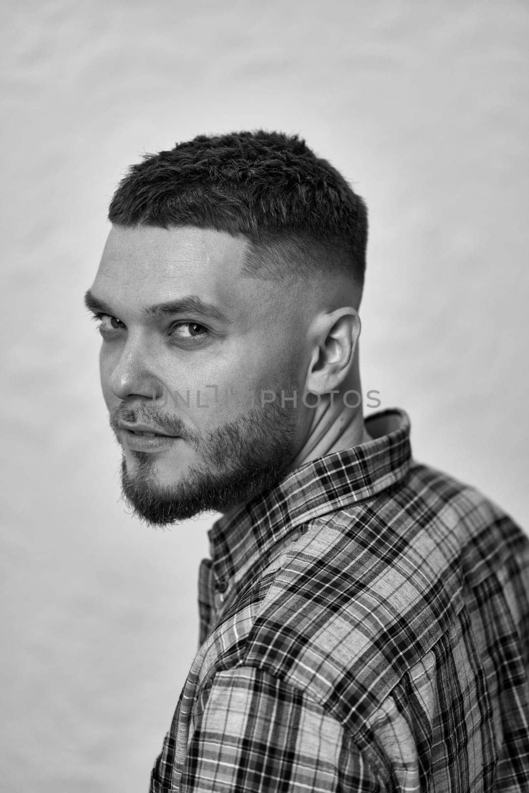 happy young man with stylish hair and beard in a plaid shirt on gray background. black and white