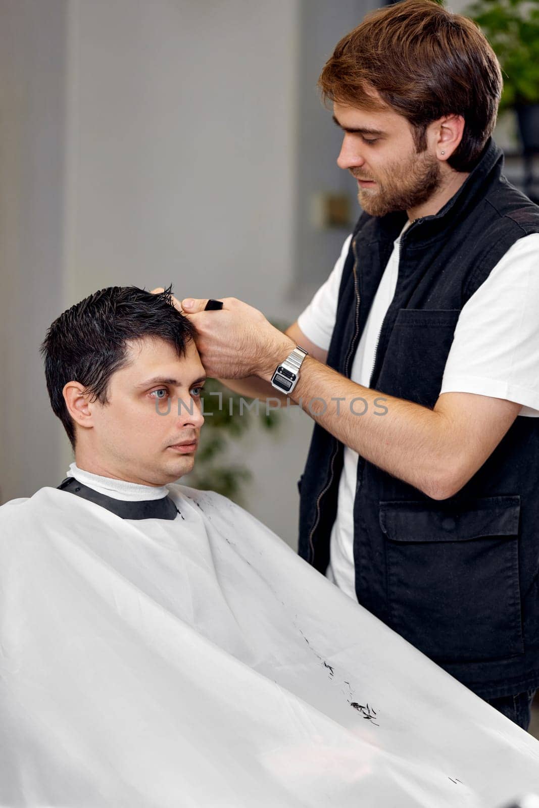 young caucasian man getting haircut by professional male hairstylist at barber shop.