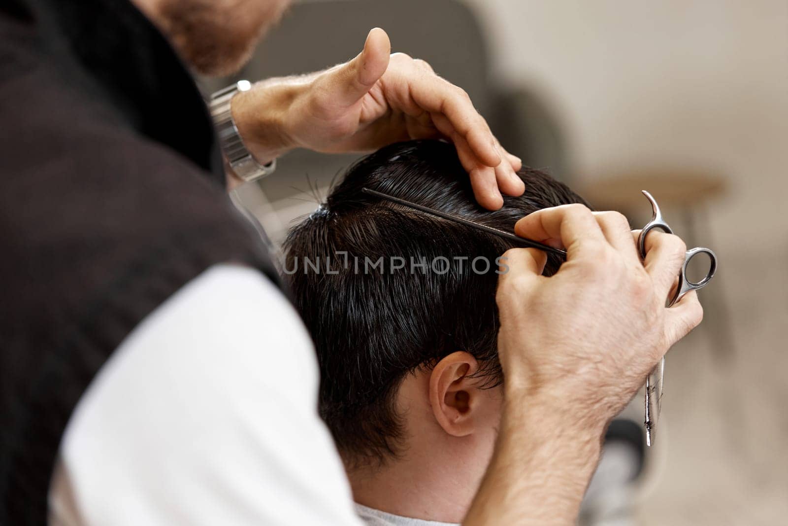 close-up, professional hairstylist does haircut for caucasian client man at barber shop.