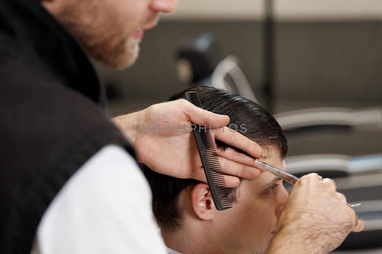 close-up, professional hairstylist does haircut for caucasian client man at barber shop.