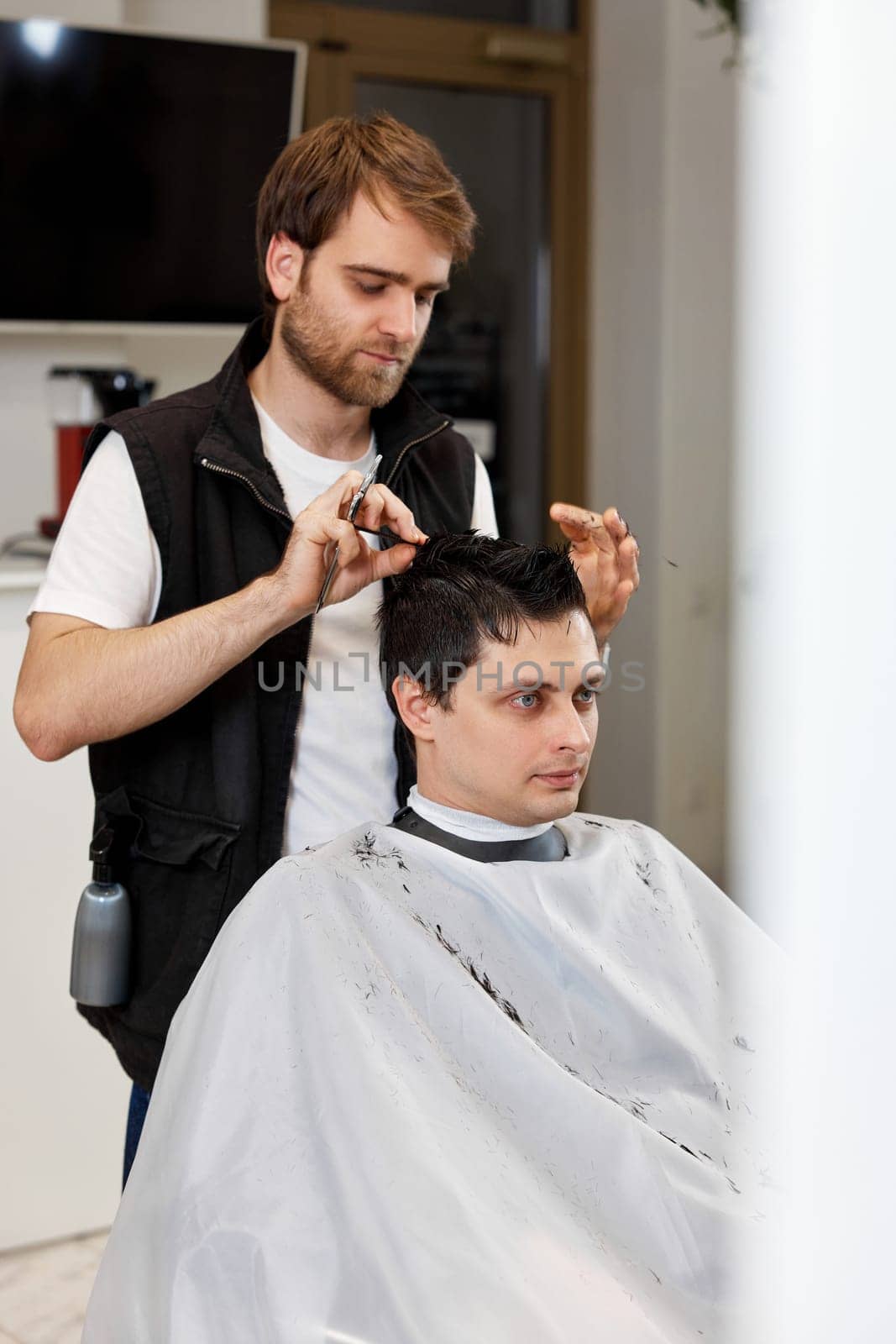 Professional hairdresser does haircut for caucasian client man at barber shop.