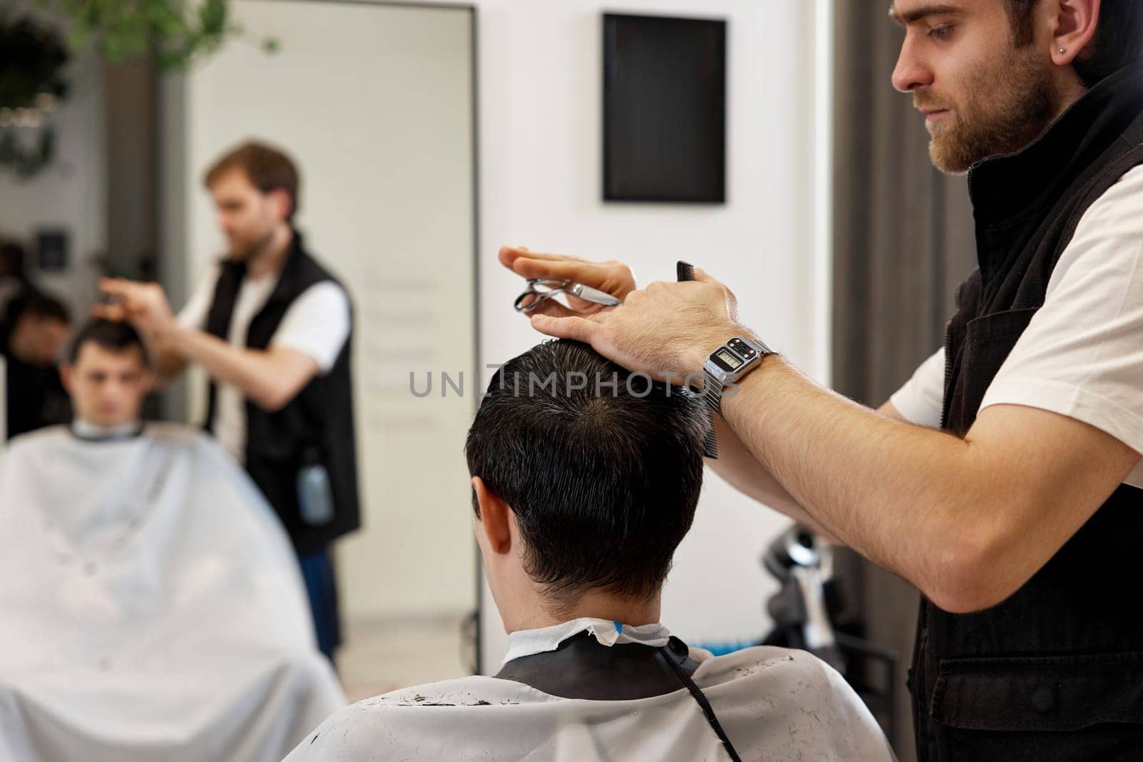 Professional hairdresser does haircut for caucasian client man at barber shop.