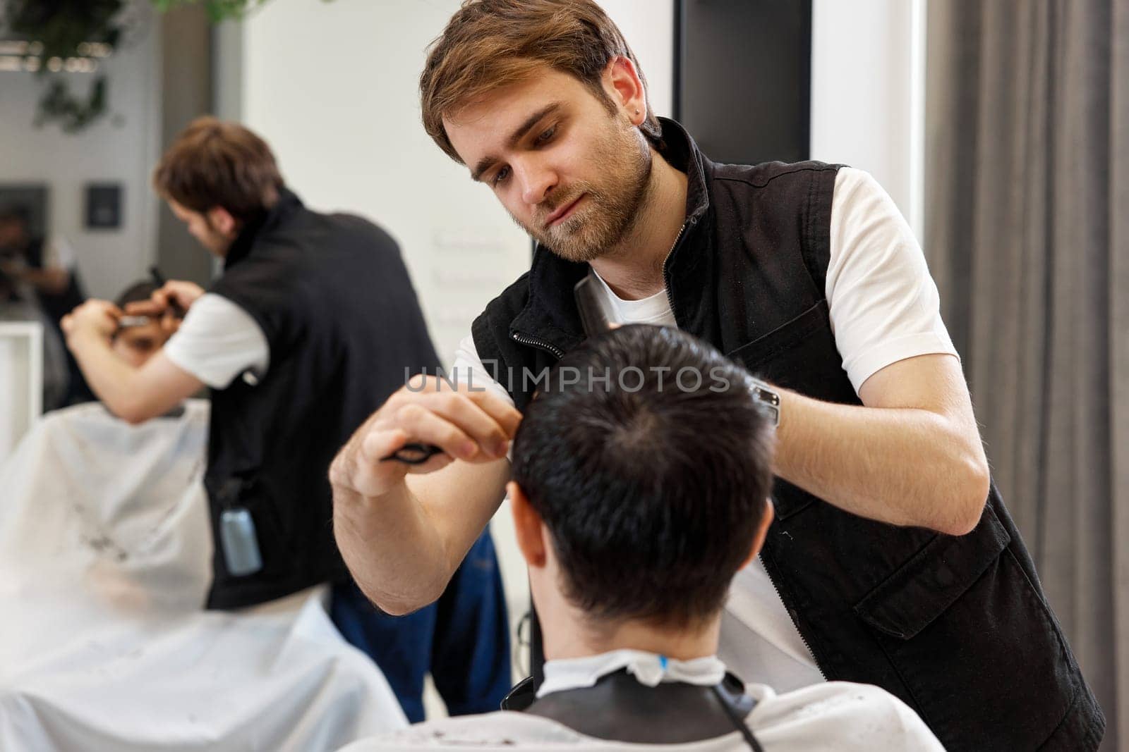 Professional hairdresser does haircut for caucasian client man at barber shop.