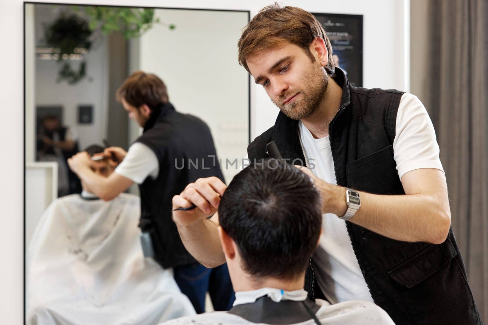 Professional hairdresser does haircut for caucasian client man at barber shop.