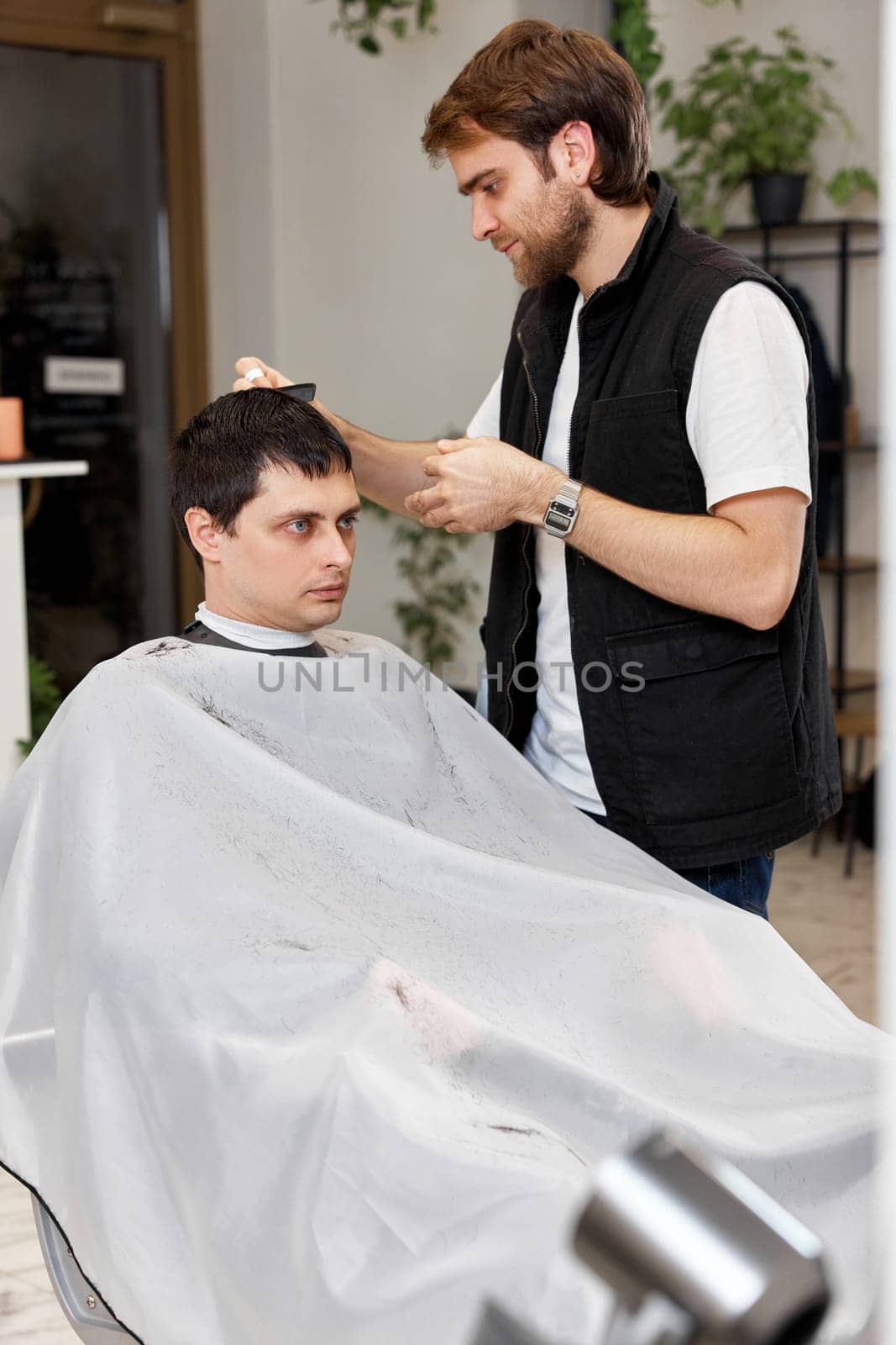 Hairstylist serving handsome caucasian man in barber shop.