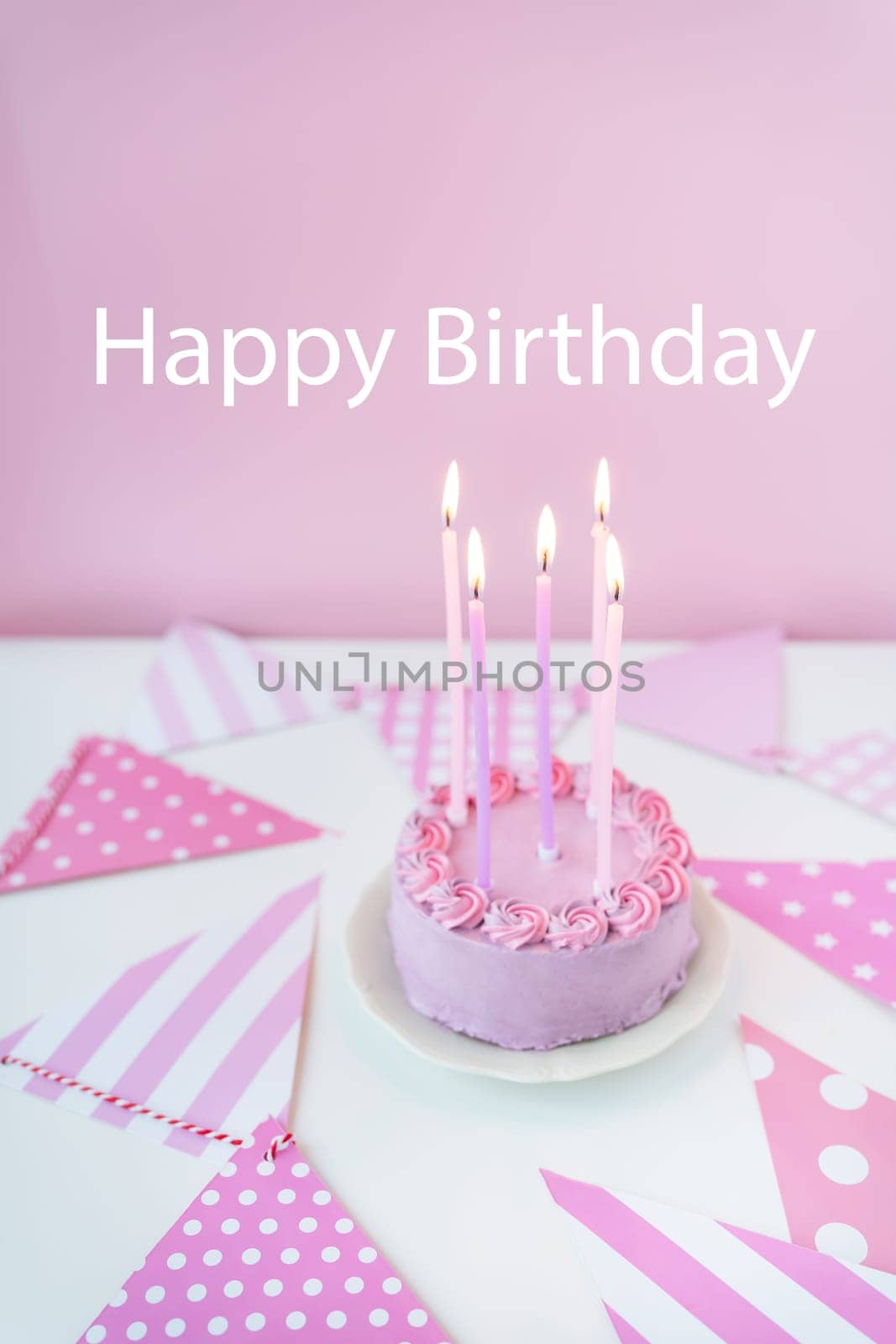 Delicate lavender pink bento cake on a plate on a pink background of party flags, candles burning on the cake. Celebration, happy birthday inscription