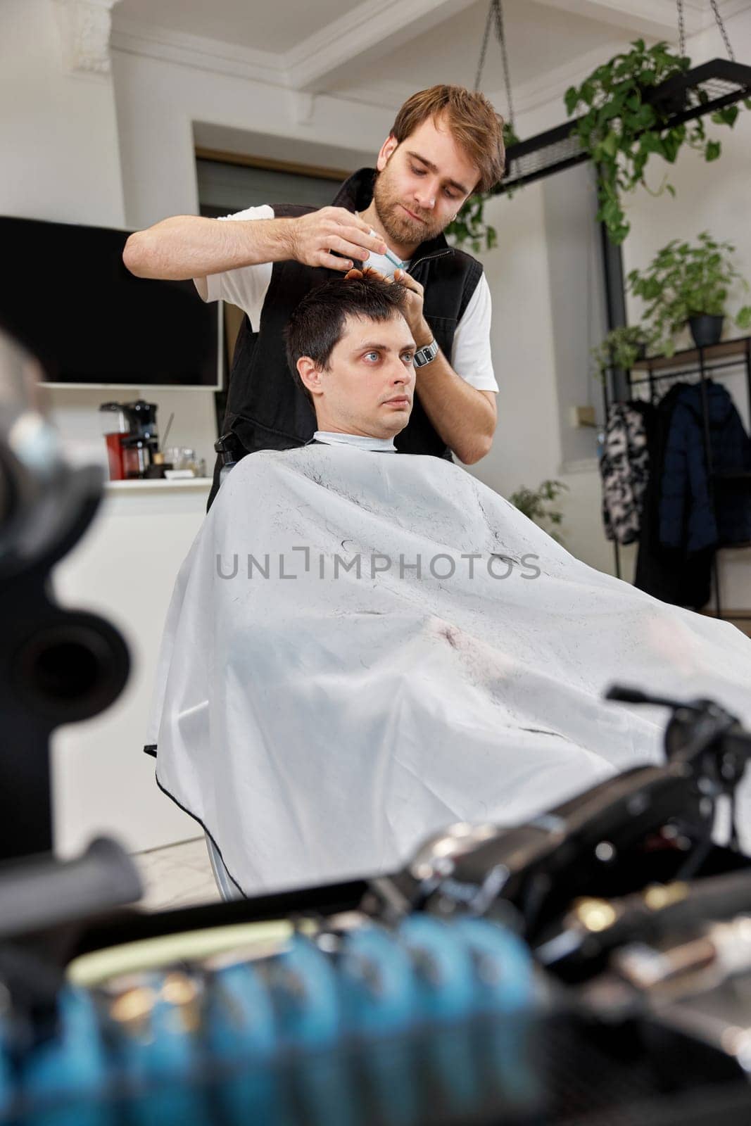Hairstylist serving handsome man in barber shop. by erstudio