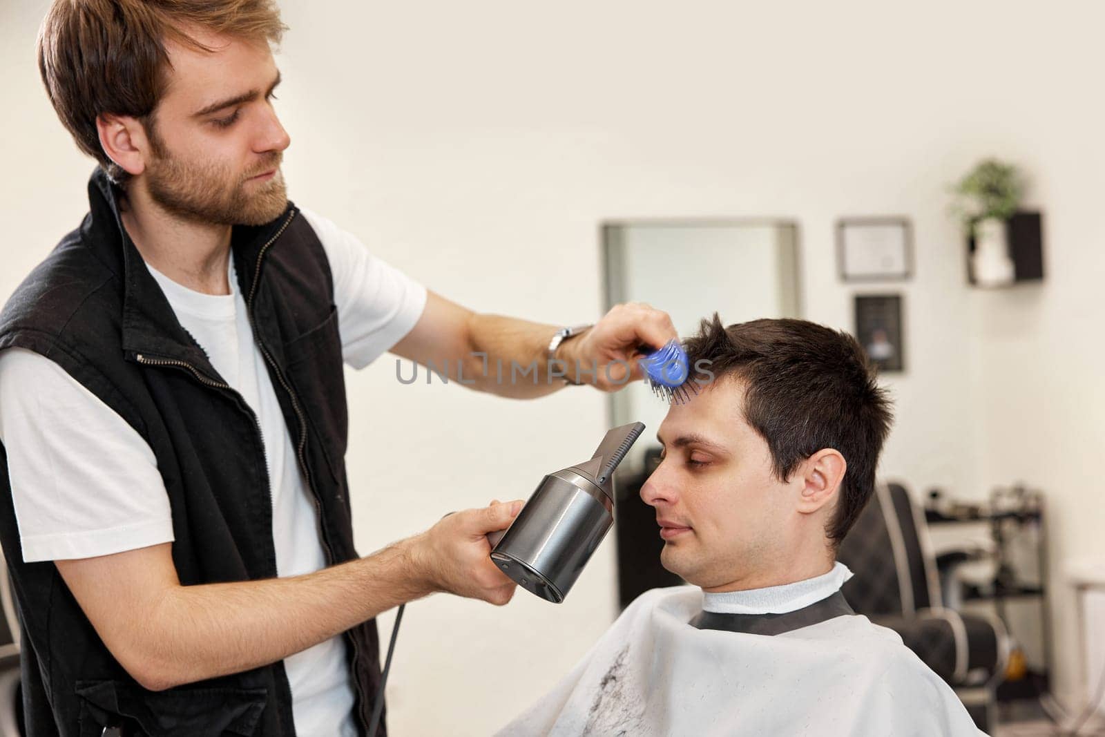 Professional hairdresser during work with man client with hair dryer in barber shop. Haircut in the barbershop.