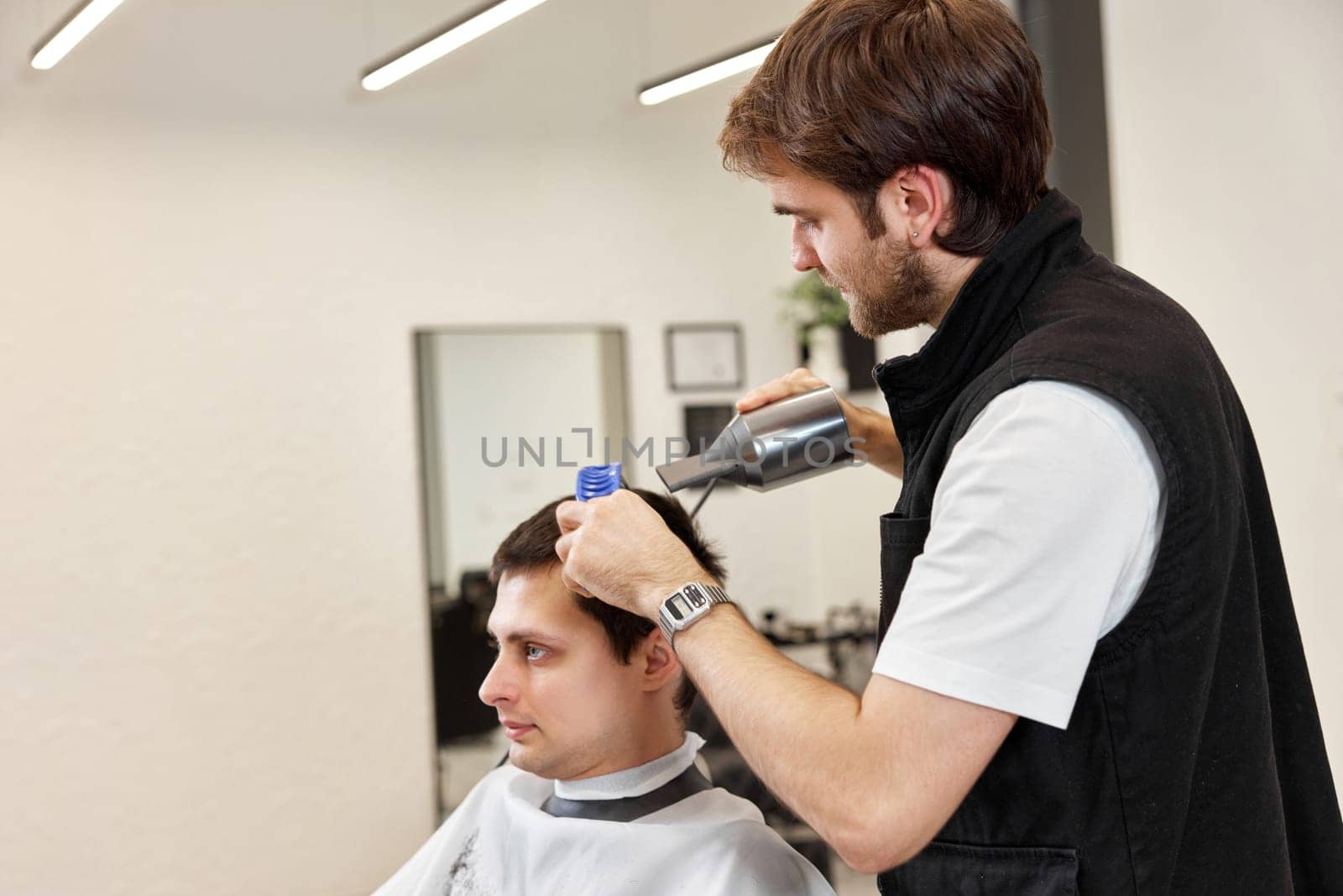 Professional hairdresser during work with man client with hair dryer in barber shop. Haircut in the barbershop.