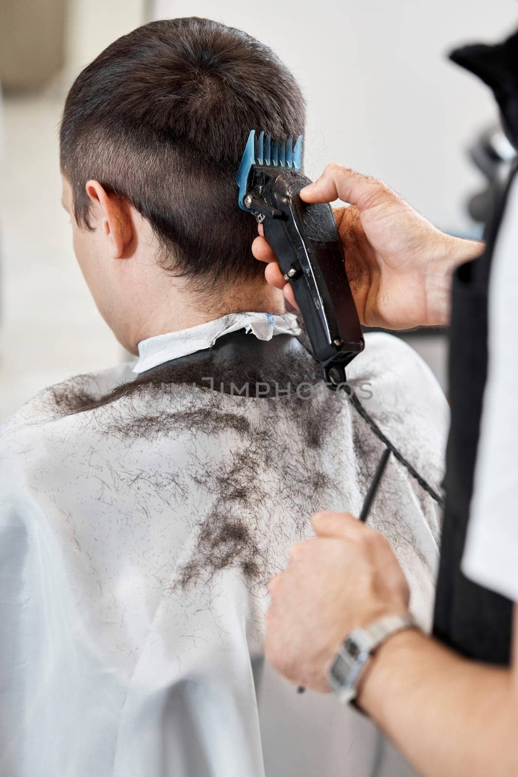 Barber trim hair with clipper on handsome man in barber shop.