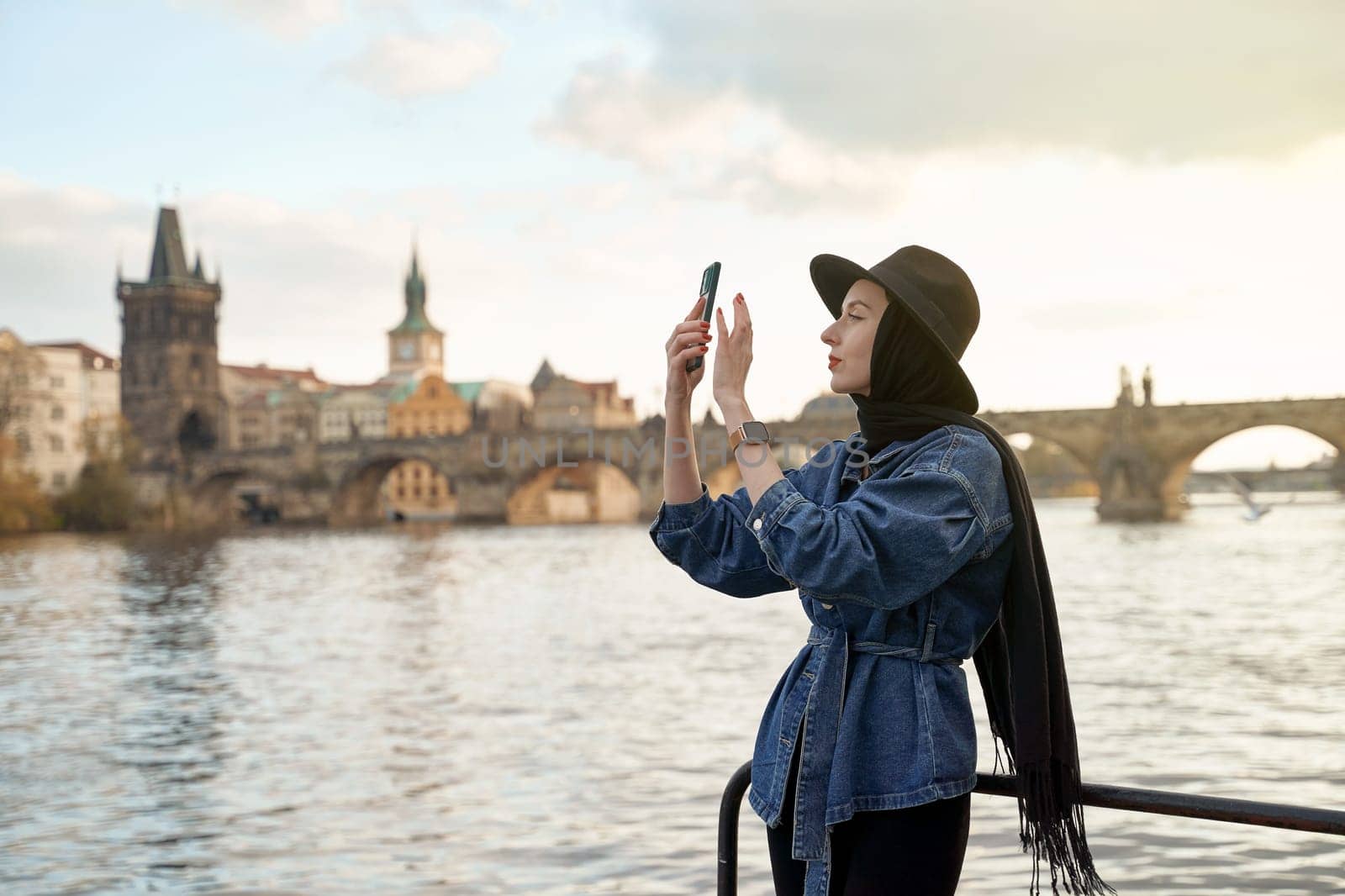 Stylish young beautiful woman earing black hat in Prague with Charles Bridge on background. Elegant retro lady fine art portrait.