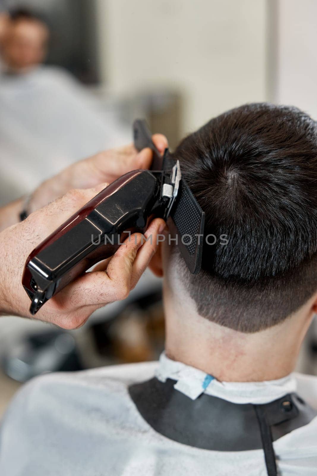 Barber trim hair with clipper on handsome man in barber shop.