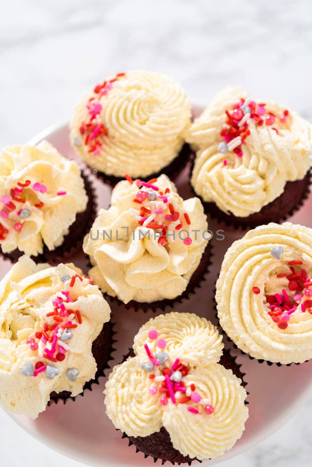 Freshly baked velvet cupcakes with white chocolate ganache frosting decorated with sprinkles.