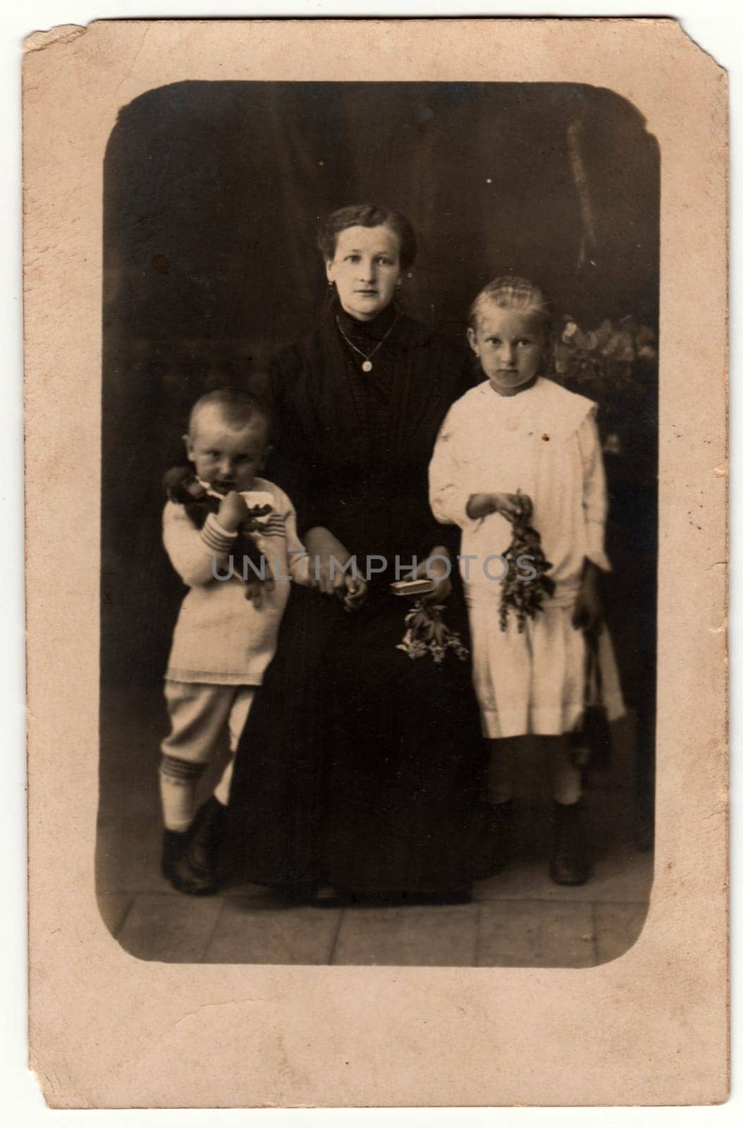 Vintage photo shows woman and her children in a photography studio. Boy wears a sailor costume and girl white dress. Retro black and white studio photography with sepia effect. by roman_nerud