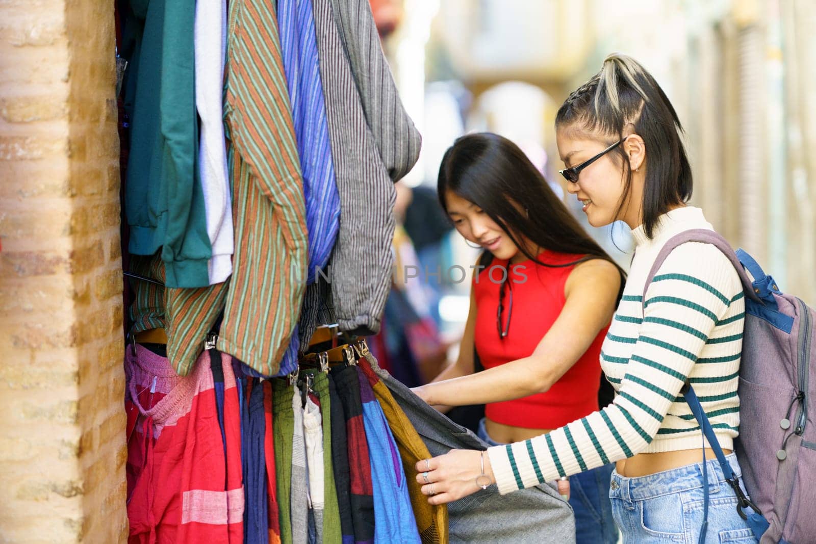 Female tourists choosing clothes in street market by javiindy