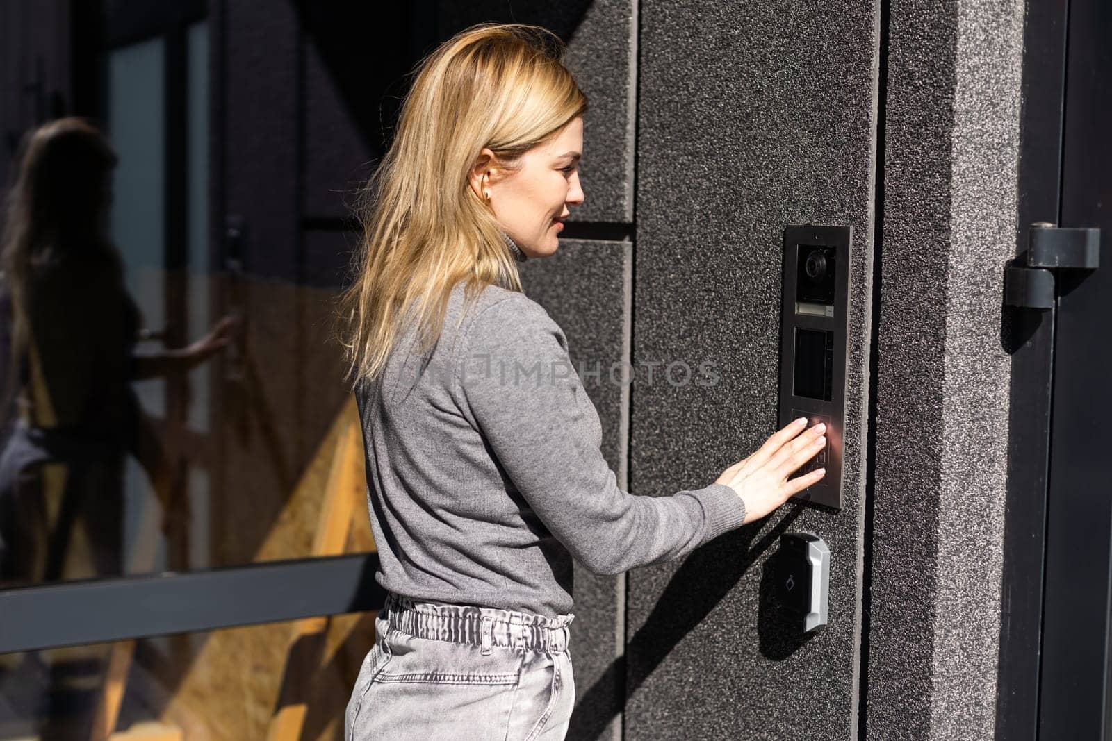 Happy woman ringing on doorbell at building entrance. Using intercom.