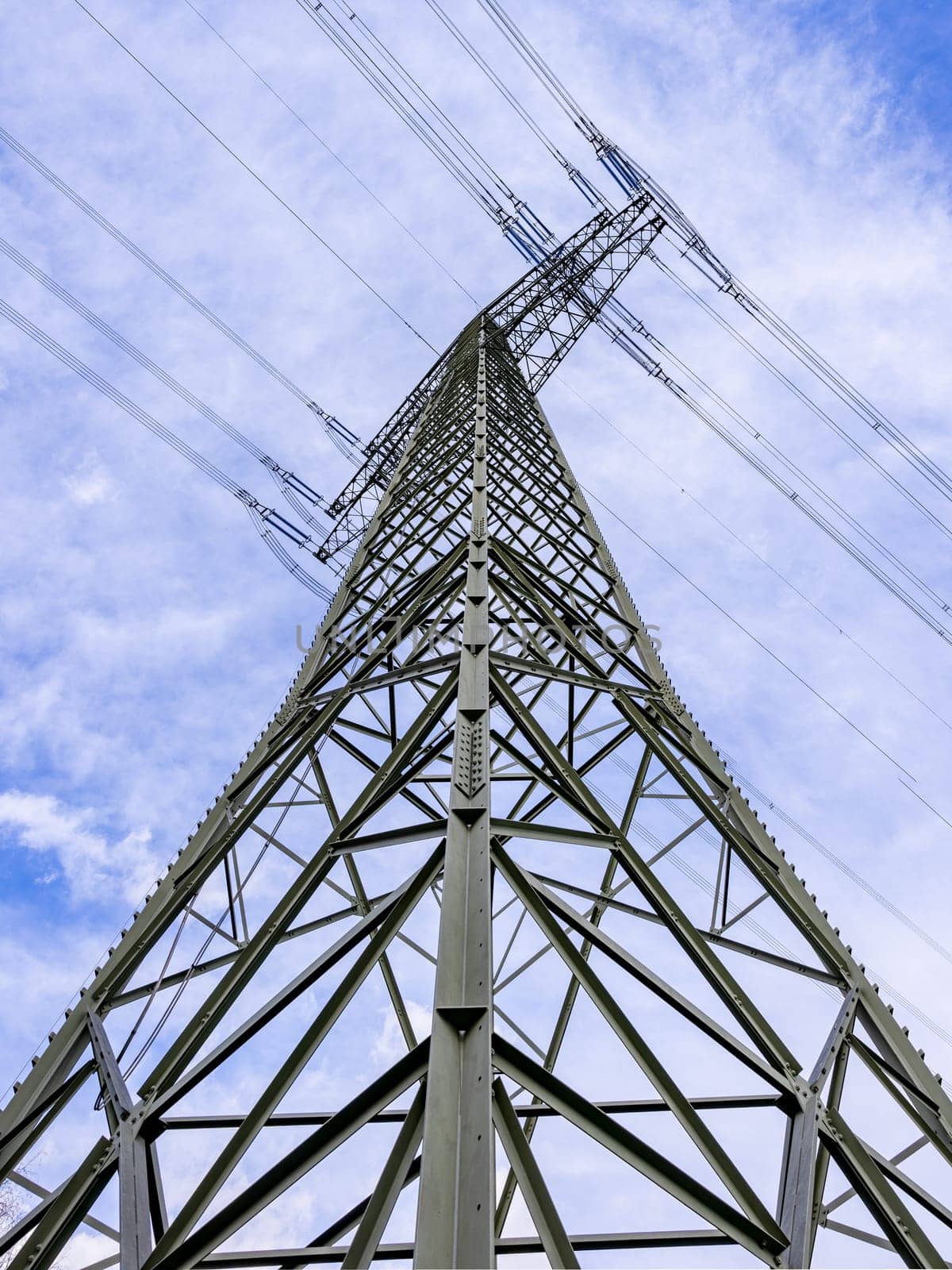 Tall steel power pole with many steel beams and struts and power lines taken from diagonal below