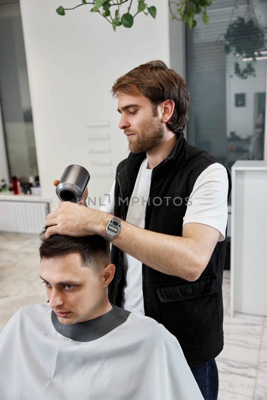 barber during work with man client with hair dryer in barber shop. Haircut in the barbershop.
