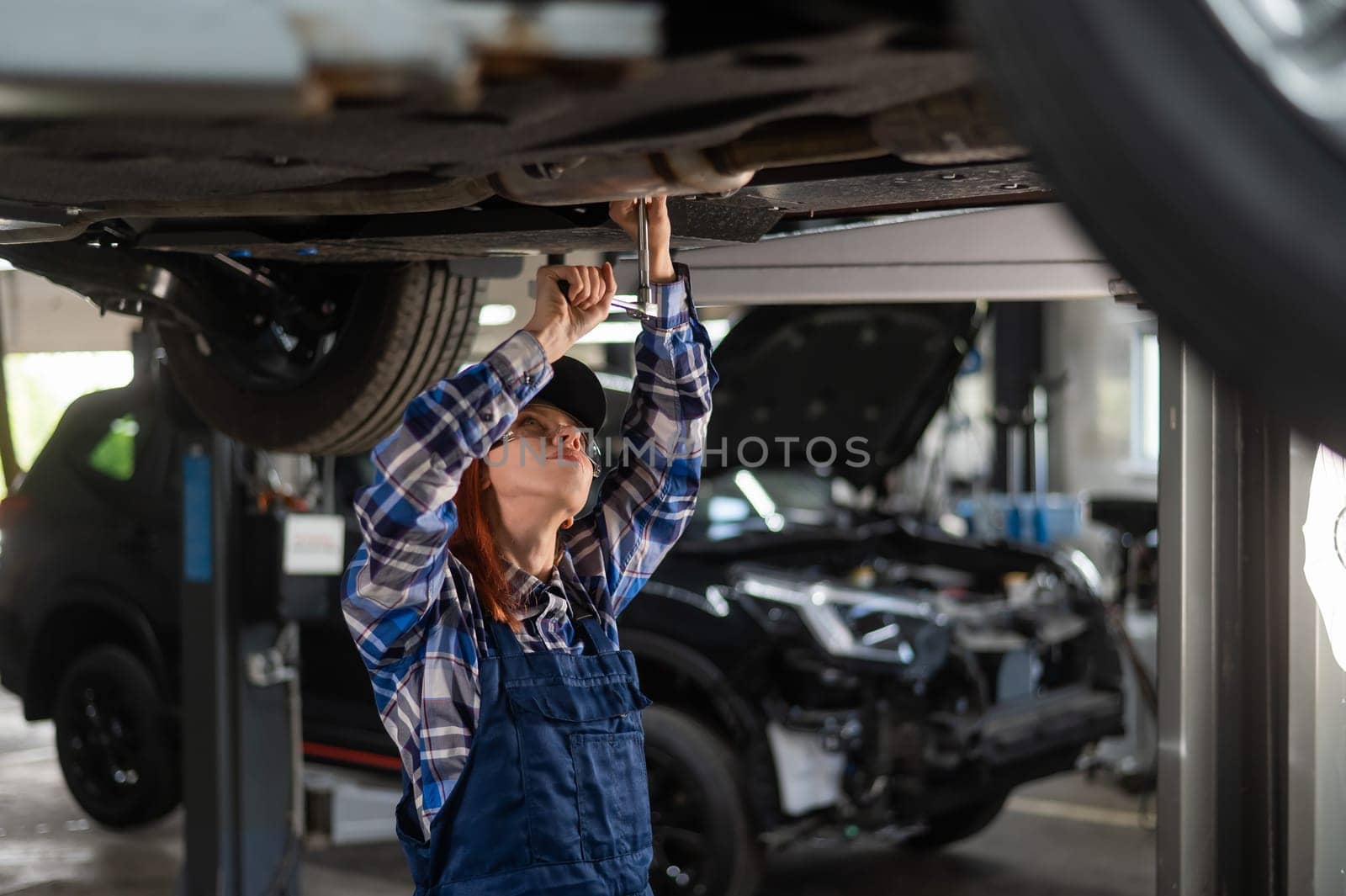 Female mechanic unscrew the nuts on the bottom of the car that is on the lift. A girl at a man's work