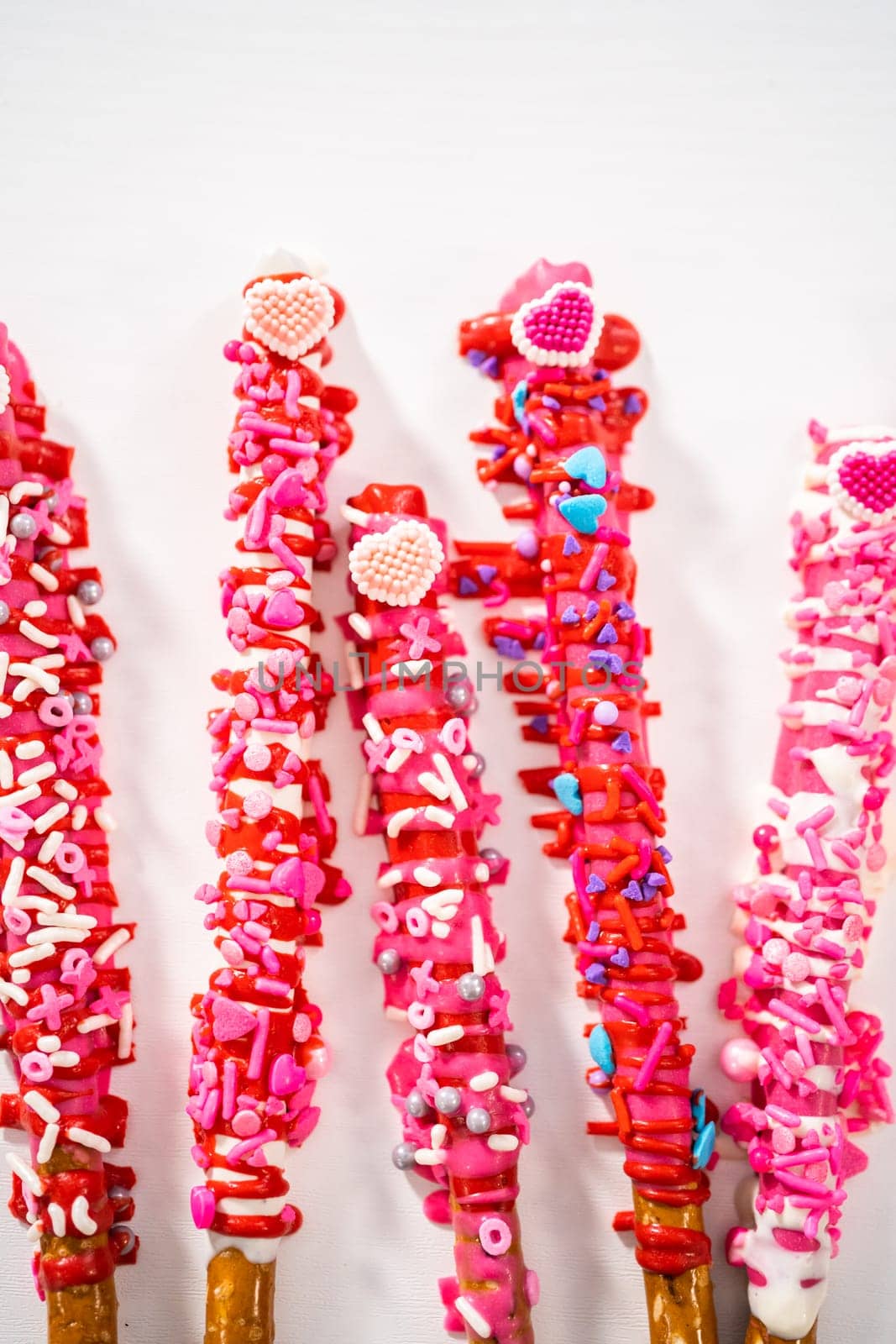 Chocolate-covered pretzel rods decorated with heart-shaped sprinkles for Valentine's Day.