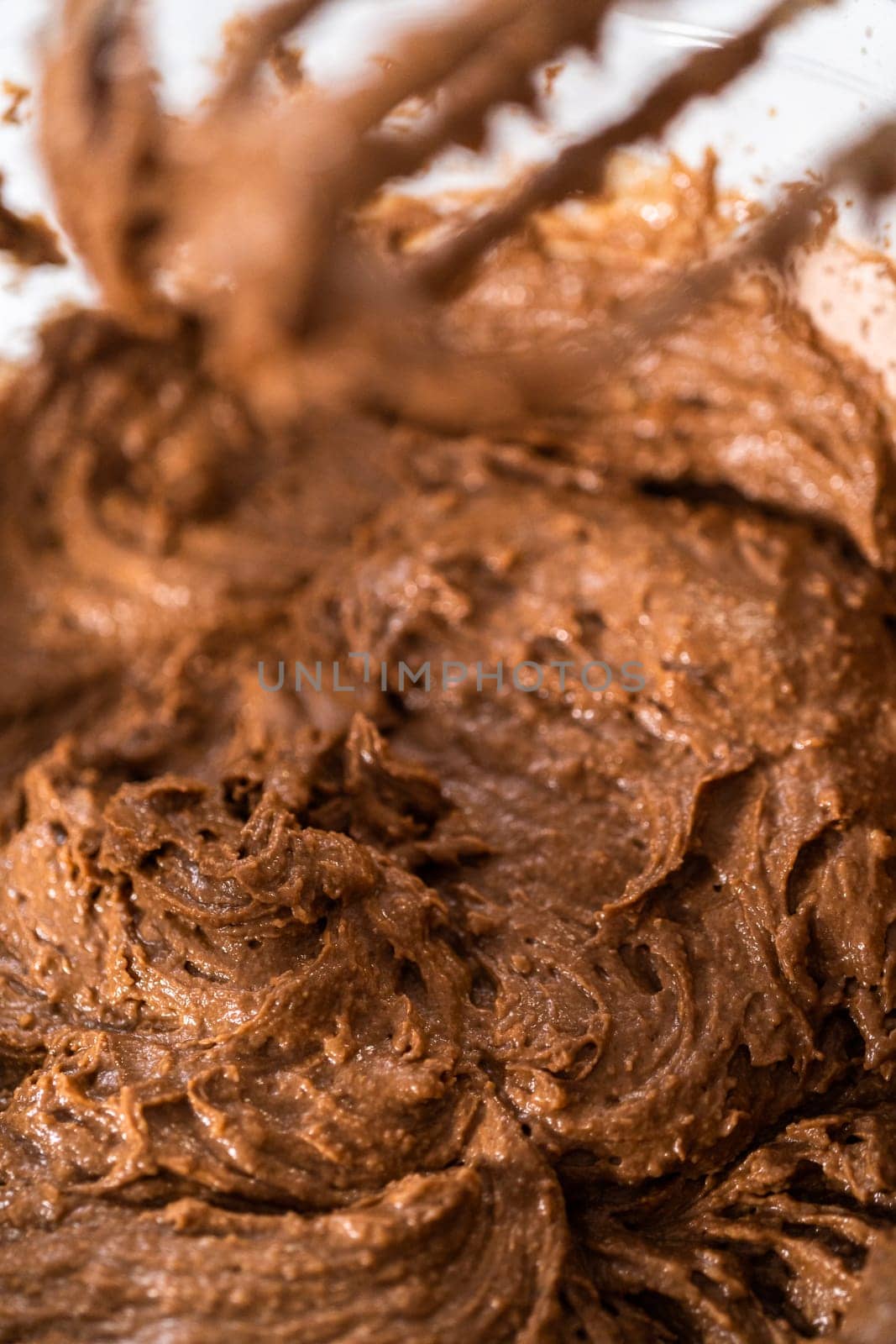 Mixing wet ingredients in a large glass mixing bowl to bake red velvet cupcakes with white chocolate ganache frosting.