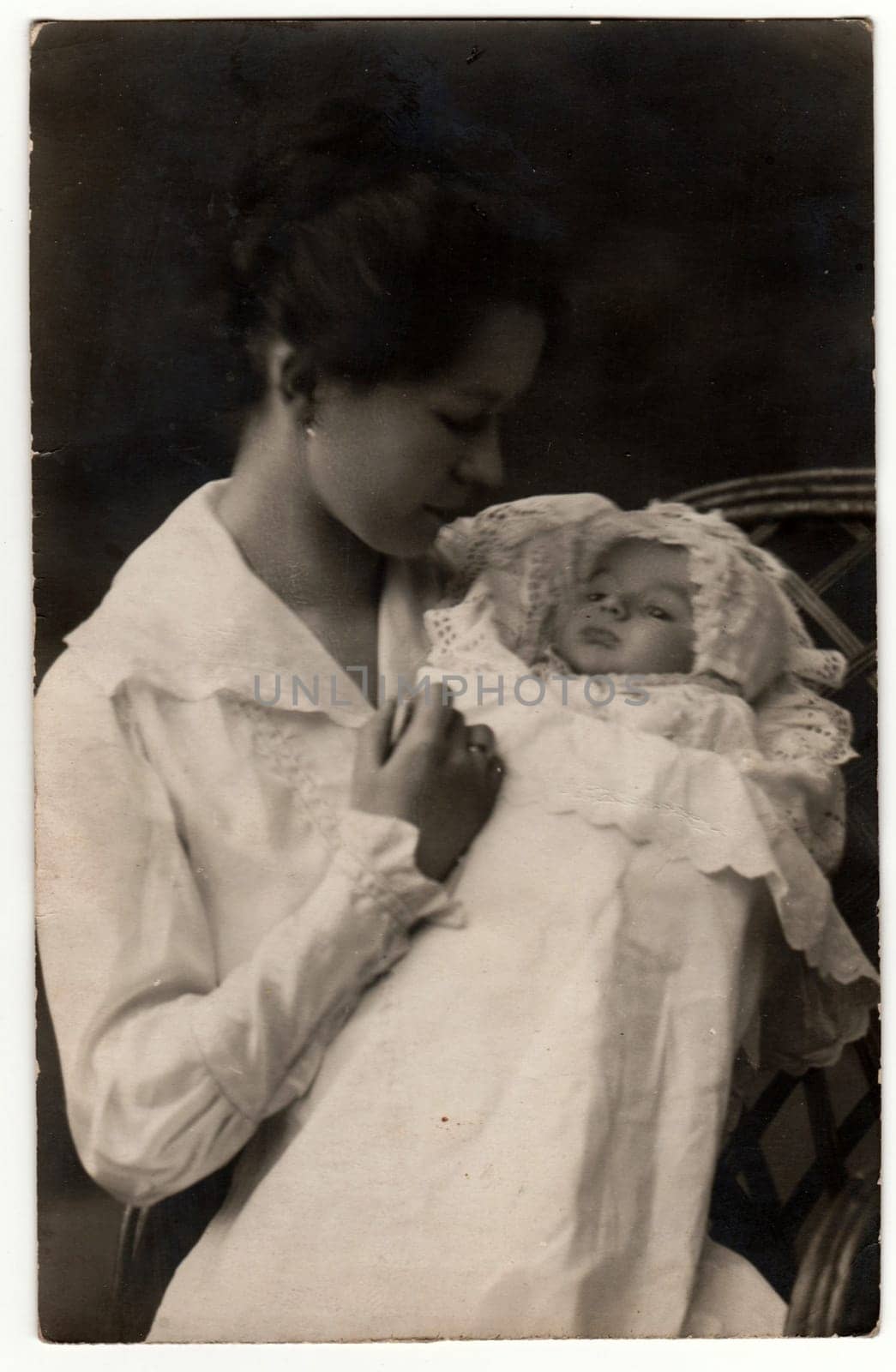 GERMANY - APRIL 25, 1918: Vintage photo shows woman with baby -newborn in swaddling clothes. Retro black and white studio photography.