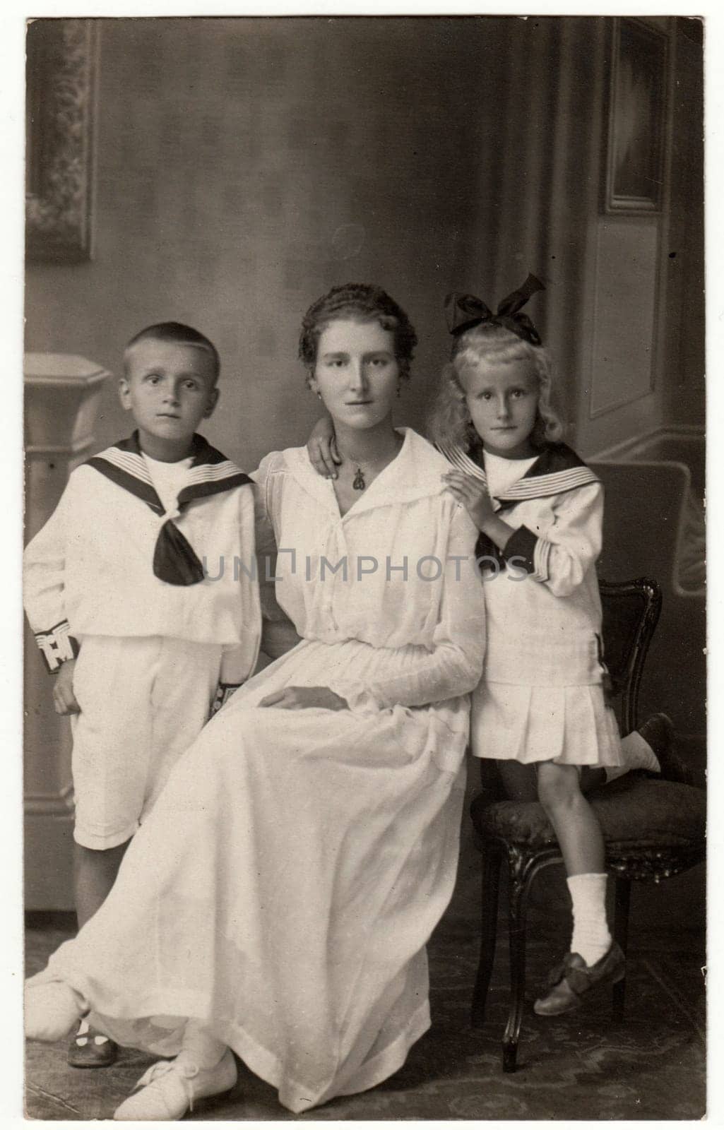 Vintage photo shows woman with her children - boy and girl. They wear sailor costumes. Retro black and white studio photography. by roman_nerud