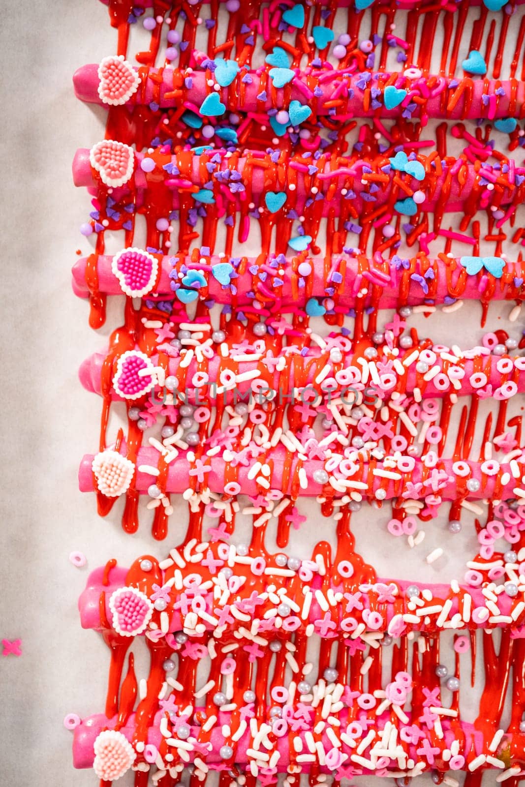Drizzling melted chocolate over chocolate-dipped pretzels rods and decorating with sprinkles to make chocolate-covered pretzel rods for Valentine's Day.