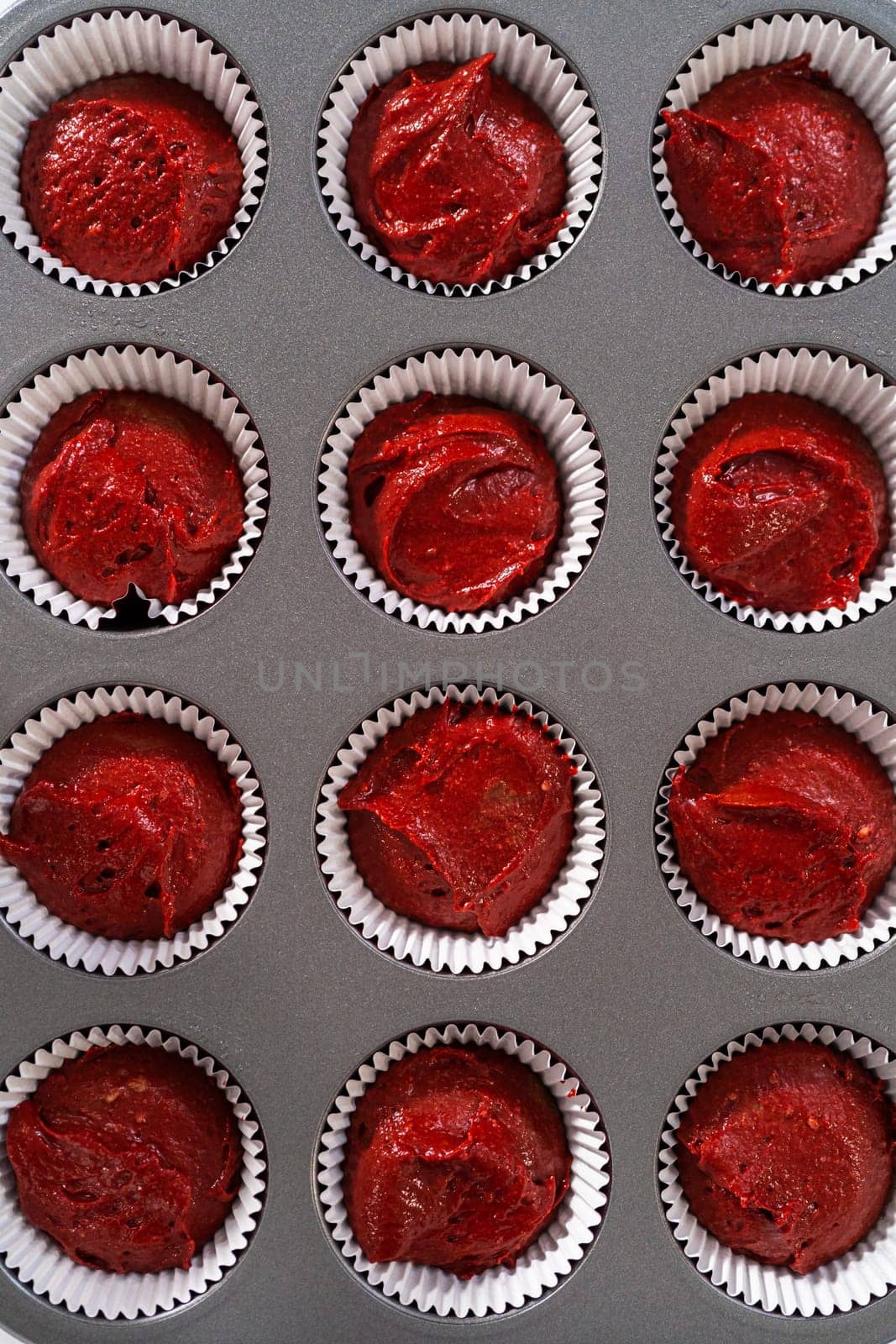 Scooping cupcake dough with dough scoop into cupcake pan lined with foil liners to bake red velvet cupcakes with white chocolate ganache frosting.