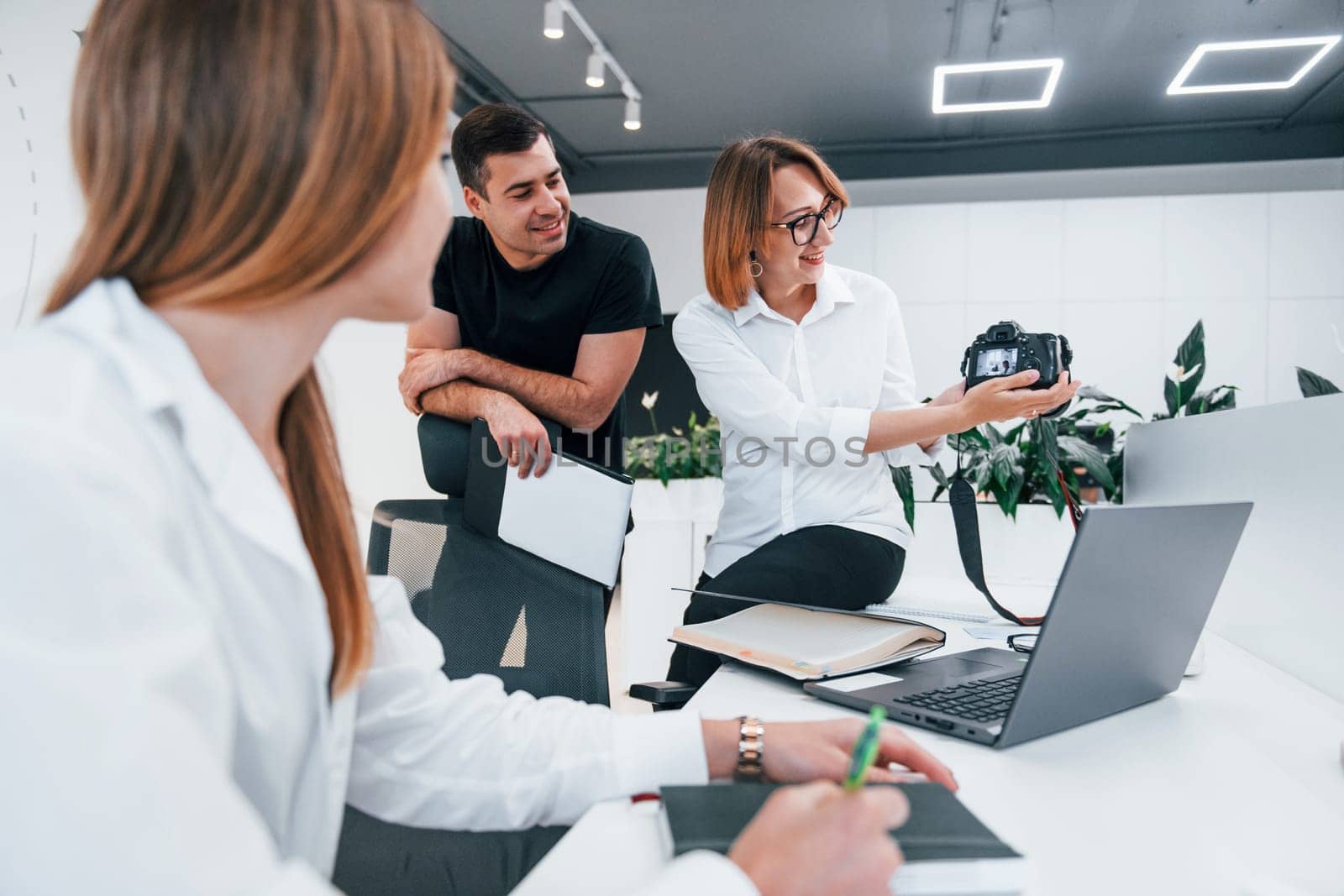 Group of business people in formal clothes indoors in the office looking at photos on the camera.