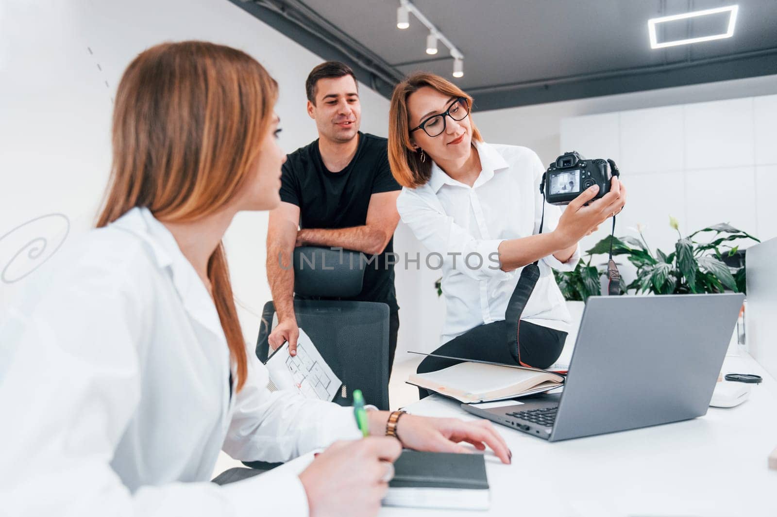 Group of business people in formal clothes indoors in the office looking at photos on the camera.