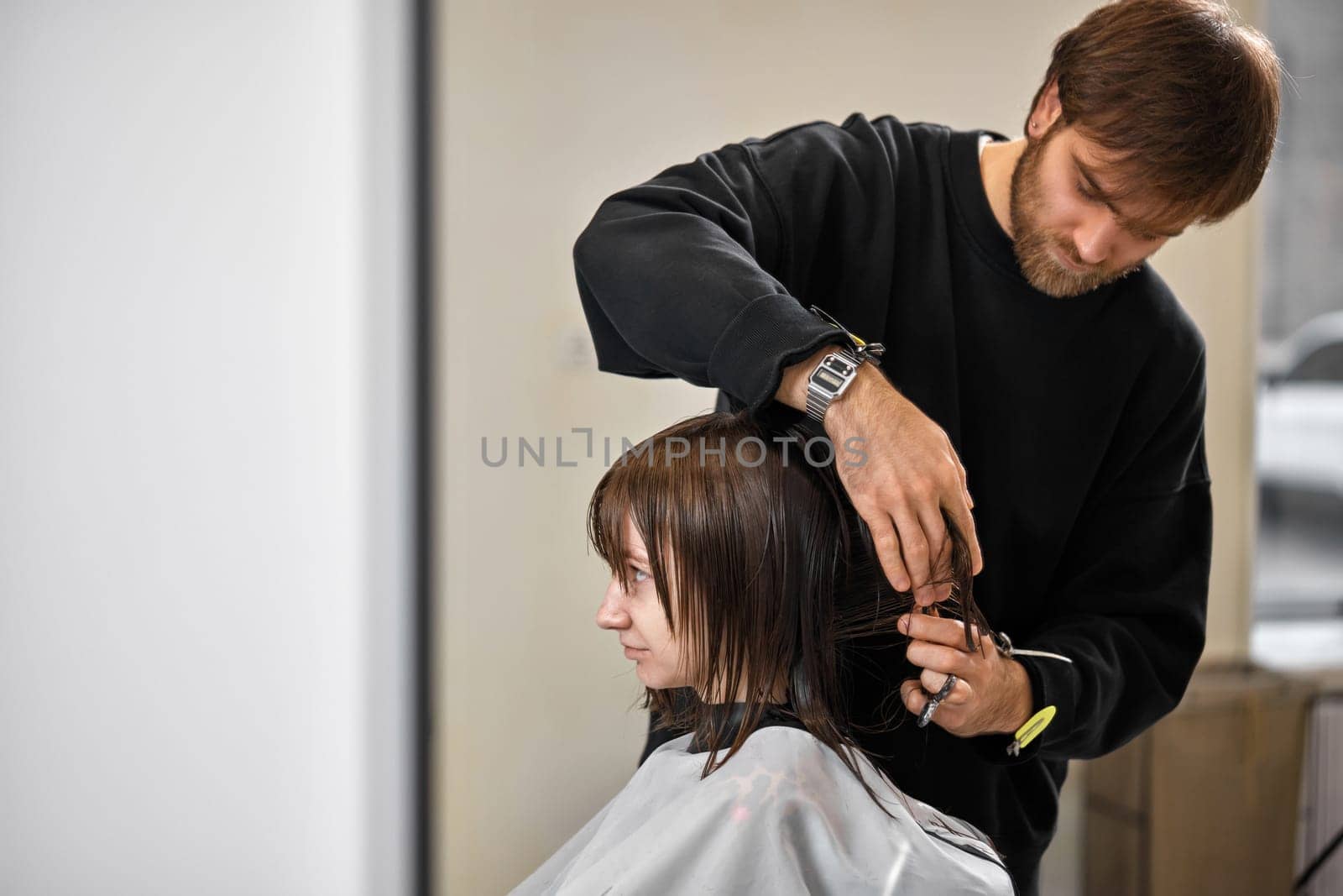 Professional male hairdresser with scissors cutting female hair in salon
