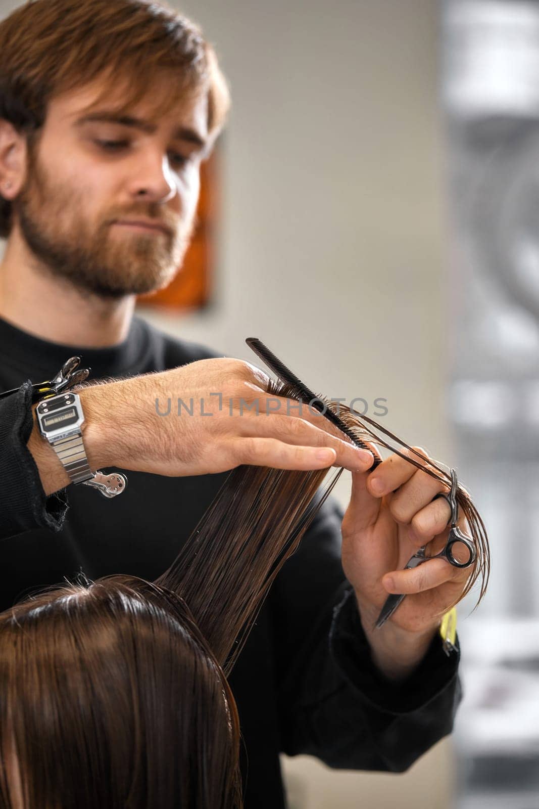 Professional male hairdresser with scissors cutting female hair in salon
