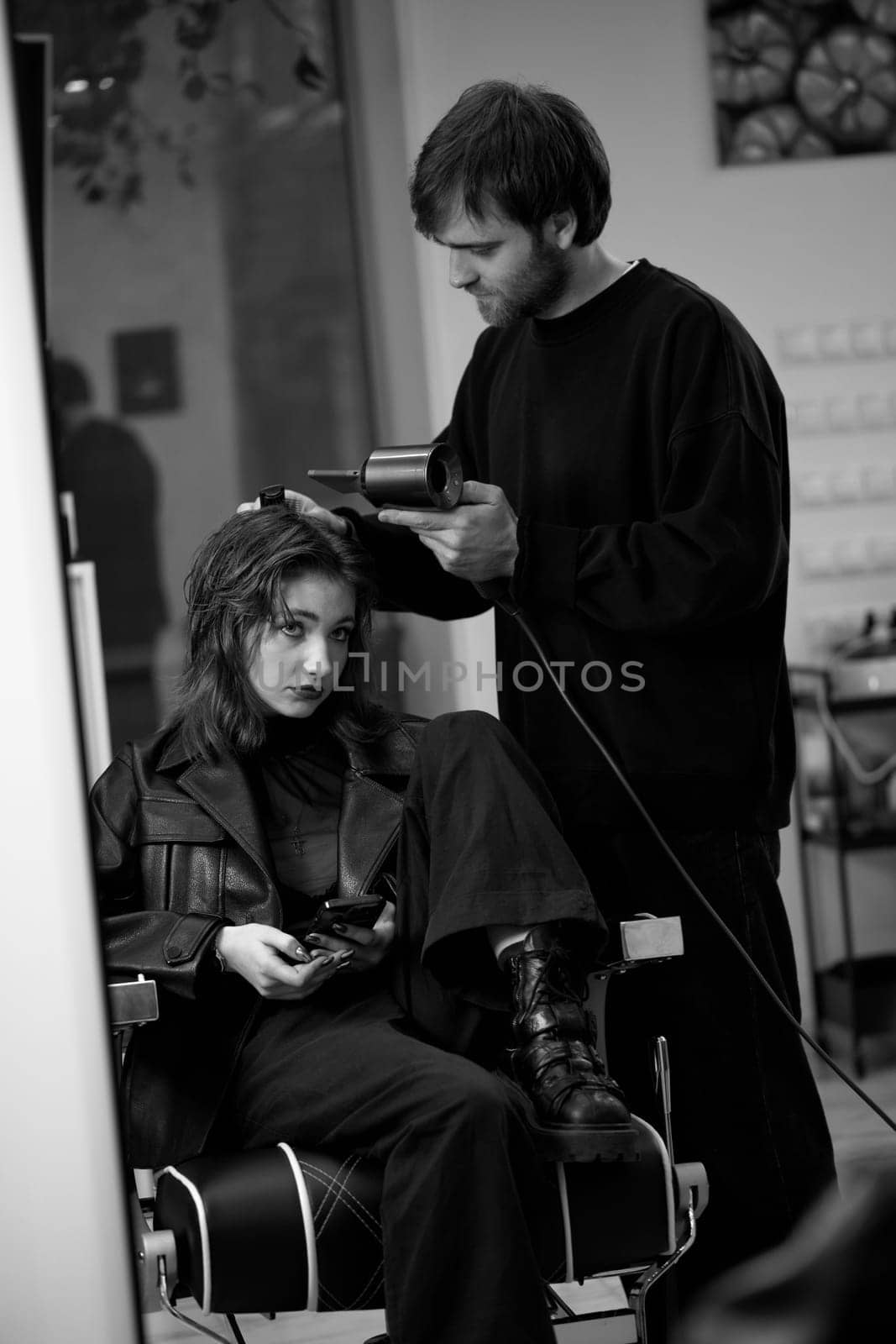 man hairdresser dries female hair with hairdryer after washing by erstudio