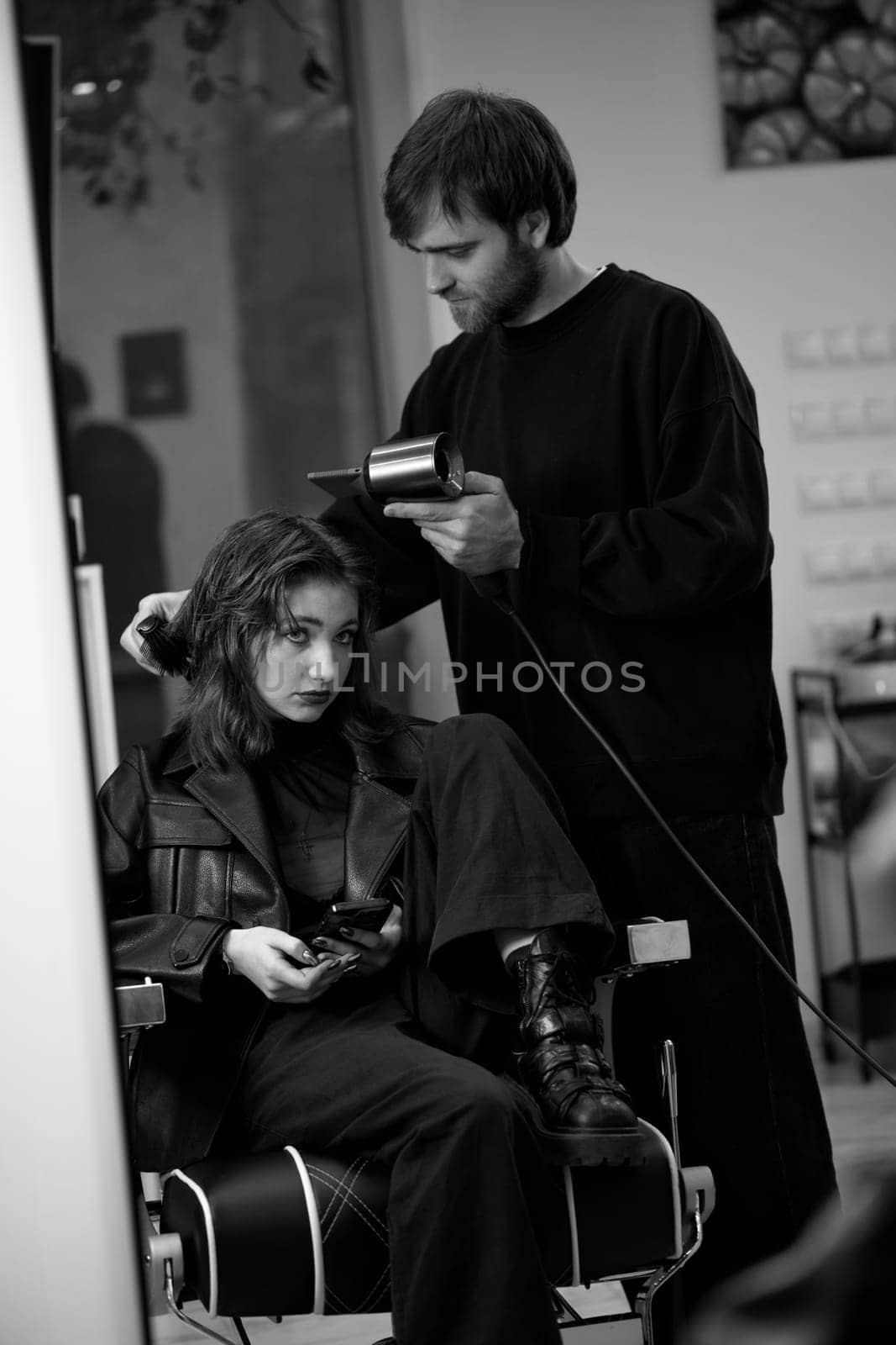 man hairdresser dries female hair with hairdryer after washing by erstudio