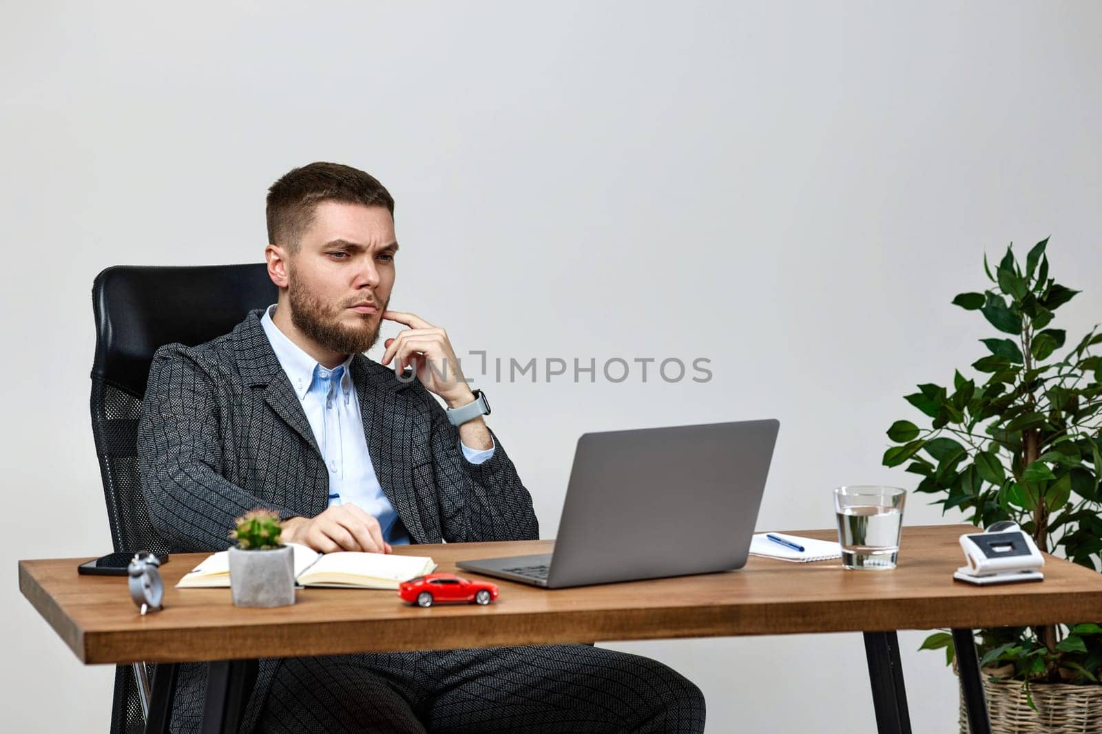 young man sitting on chair at table and resting, using laptop on white wall background