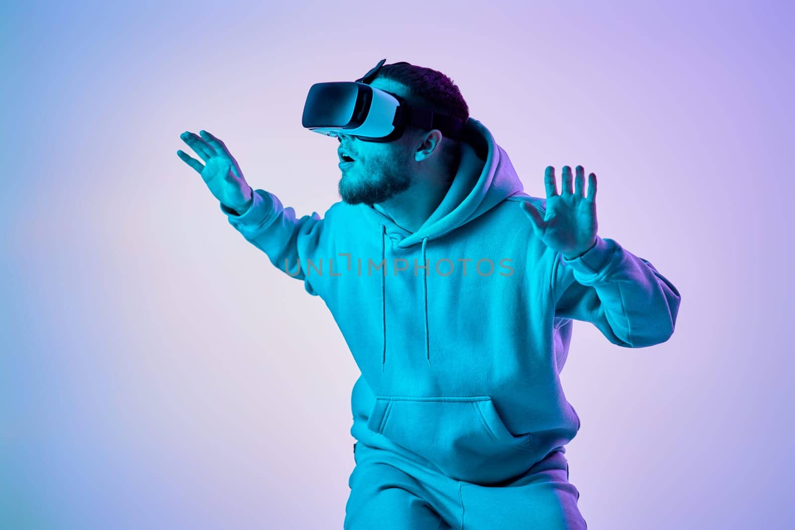 man in sweatshirt using virtual reality glasses and playing video games on blue background. Neon lighting