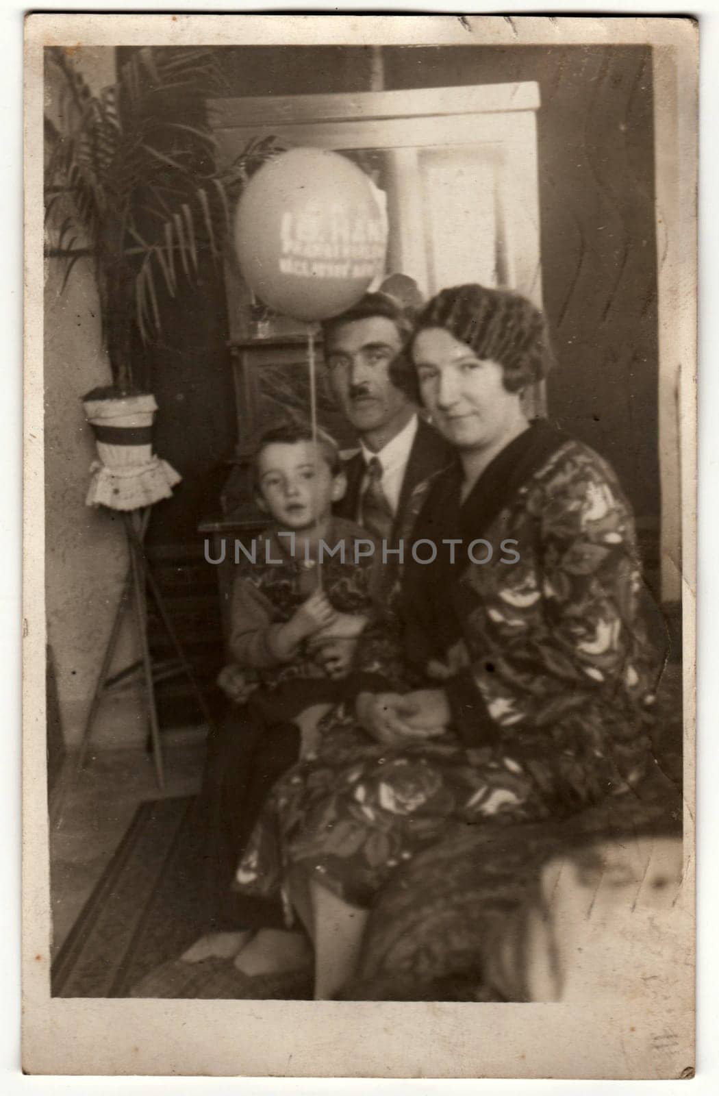 Vintage photo shows family in the living room. Boy holds air-ball - inflatable ball. Retro black and white photography. Circa 1930s. by roman_nerud