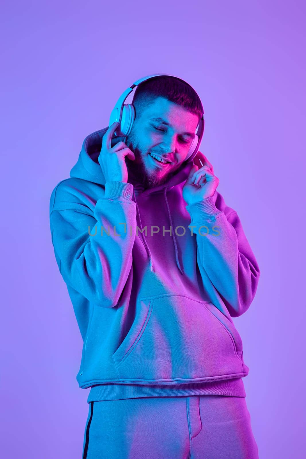 handsome bearded man with headphones in sweatshirt enjoying favorite music on purple neon background. Neon lighting