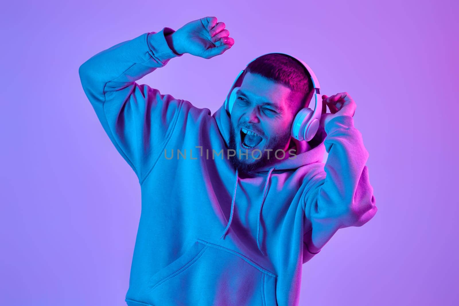 handsome man listening to music with wireless headphones on purple neon background. Neon lighting