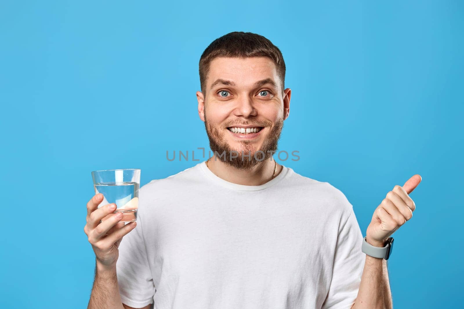 bearded man with drinking glass of water pointing to the side on blue background