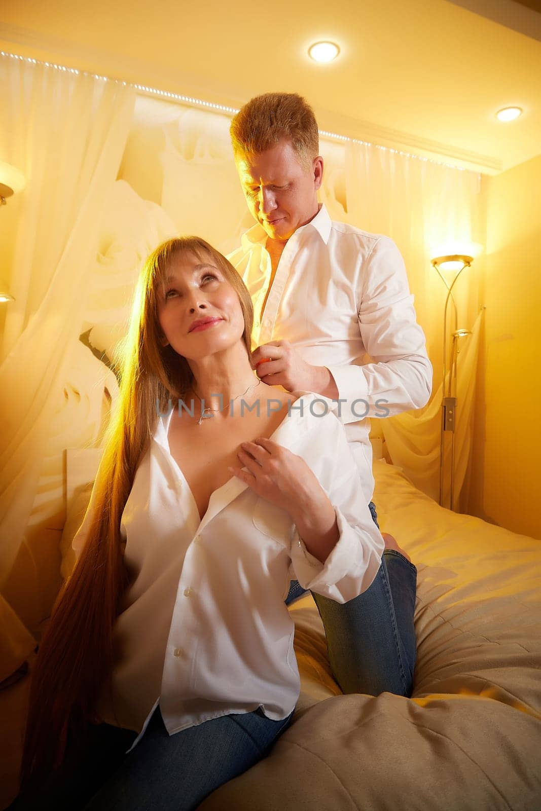 An adult couple of newlyweds in in white shirts in a hotel room after the wedding. A guy and a girl, a man and a woman in beautiful room. The concept of love and care
