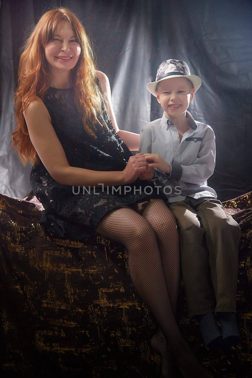 Woman with boy in hat. Mom with son on a dark background. Family portrait with mother with red hair and boy having fun together