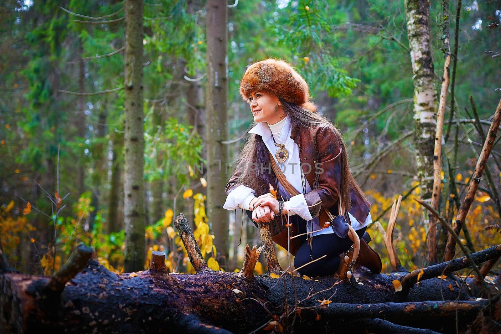 Girl in a leather jacket, a big red fox fur hat in the forest in autumn. A female model poses as a fabulous royal huntress on nature hunt at a photo shoot