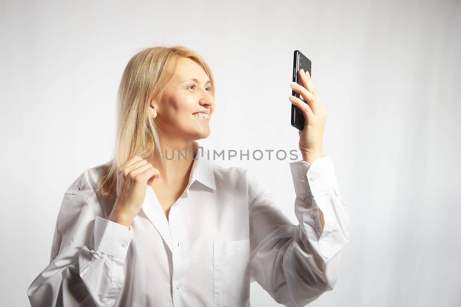 Portrait of a smiling casual woman holding smartphone over white background. The girl is chatting and taking selfies. Business lady with cell phone. Copy space